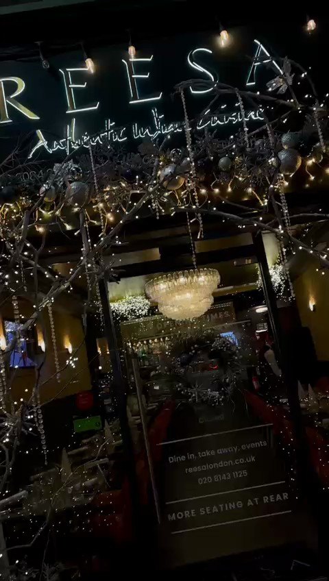 The Reesa restaurant entrance at night, the illuminated sign above a canopy of
                    frosted branches, glass baubles and hanging crystal snowflakes.