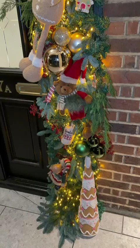 A lit door garland hung with gold and green baubles, candy canes and gingerbread figures.