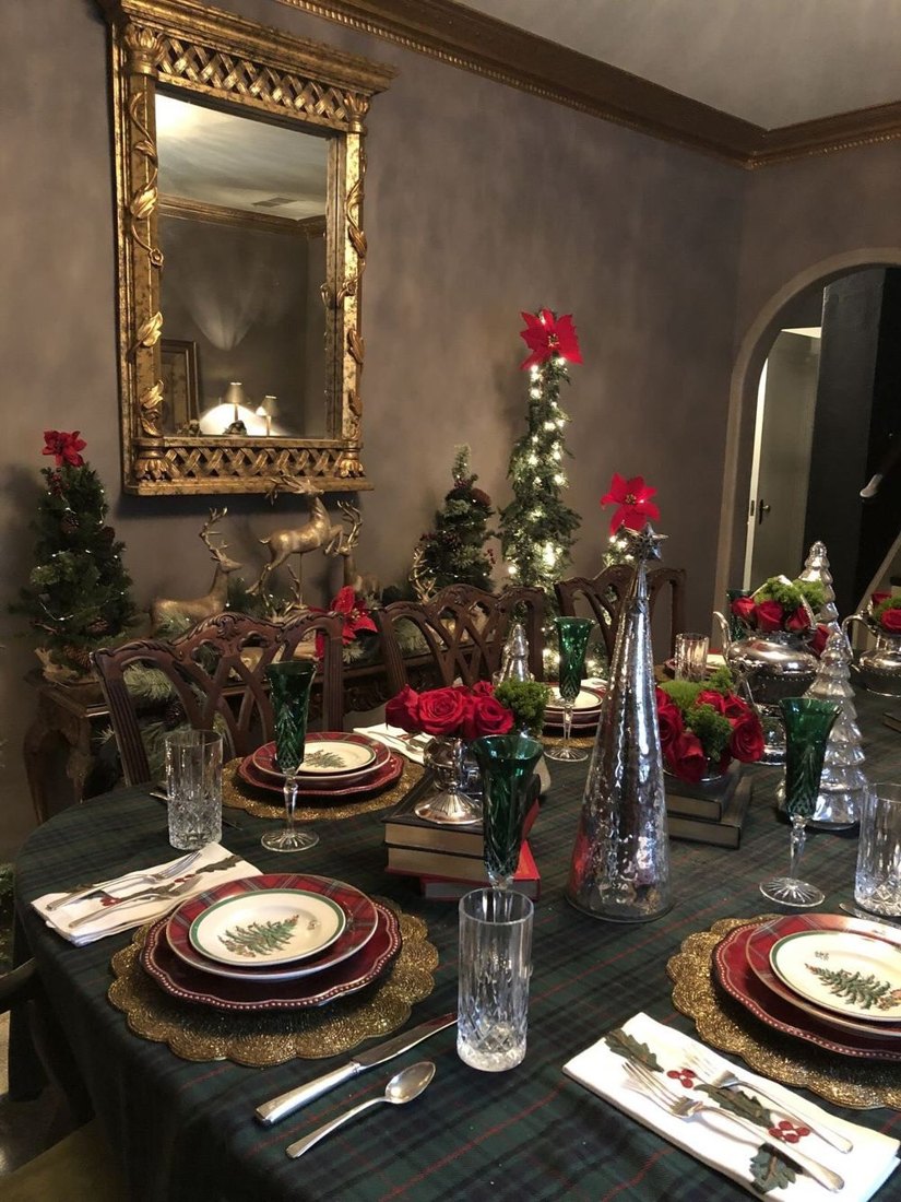 A Christmas dinner table on tartan cloth with gold chargers, red and green
                    place settings, candles, miniature lit trees and poinsettia.