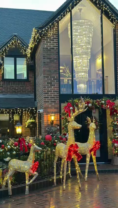 A lit building frontage at dusk with illuminated reindeer, garlanded railings and
                  warm lantern light beside the entrance.